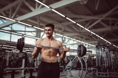 Genç adam spor salonunda halterle kaslarını esnetiyor.