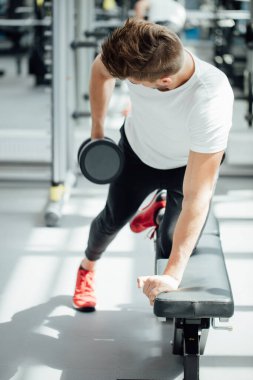 Spor salonunda dambılla çalışan güçlü bir adam.