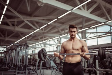 Genç adam spor salonunda halterle kaslarını esnetiyor.