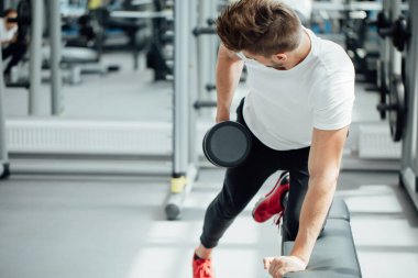 Spor salonunda dambılla çalışan güçlü bir adam.