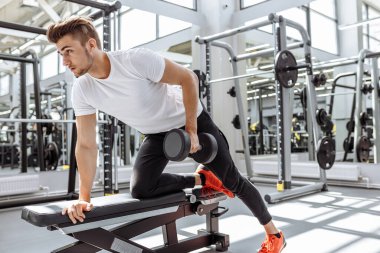 Spor salonunda dambılla çalışan güçlü bir adam.