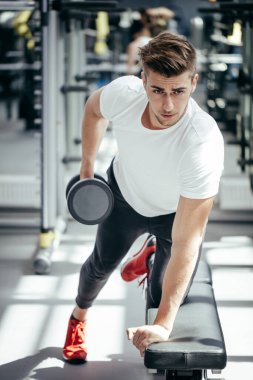 Spor salonunda dambılla çalışan güçlü bir adam.