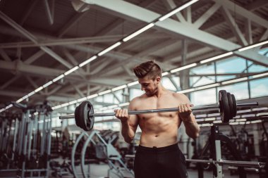 Genç adam spor salonunda halterle kaslarını esnetiyor.