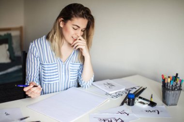 Genç ve güzel bir bayan beyaz masada oturuyor ve kaligrafiyi düşünüyor.