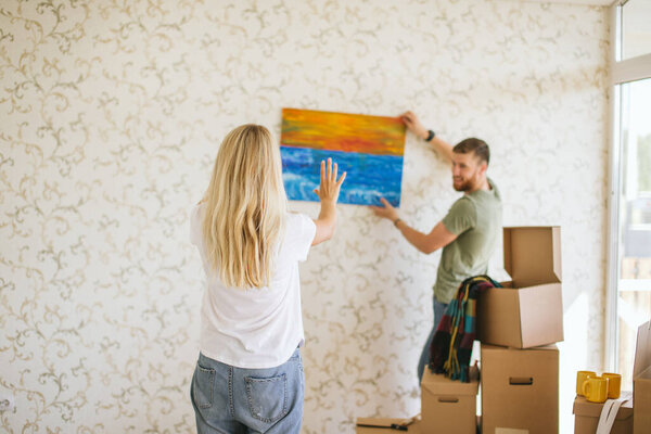 Moving house. Couple hanging picture on wall in new home