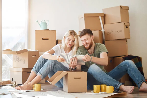 Pareja con libro sentado en la cama mientras se muda a un nuevo hogar — Foto de Stock