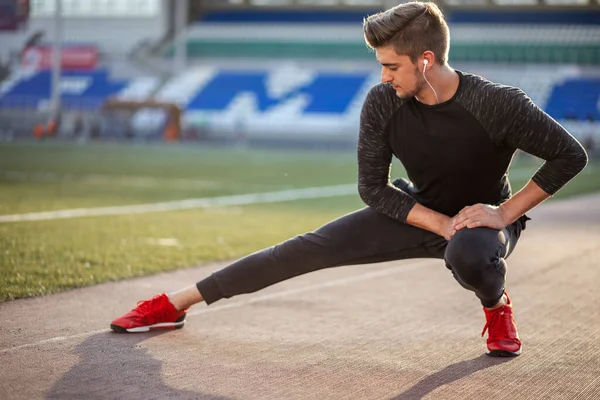 Hombre estira el cuerpo antes de correr en pista de carreras en el estadio —  Fotos de Stock