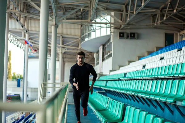 Hombre en forma vistiendo ropa negra corriendo arriba en el estadio deportivo —  Fotos de Stock