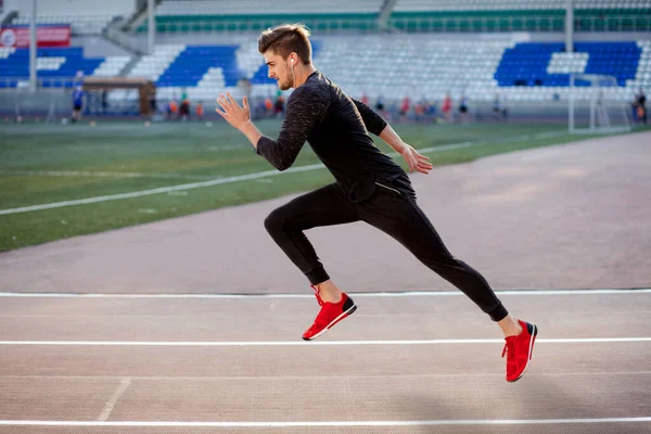身穿黑色运动鞋的男子运动员在跑道上跑，侧面看 — 图库照片
