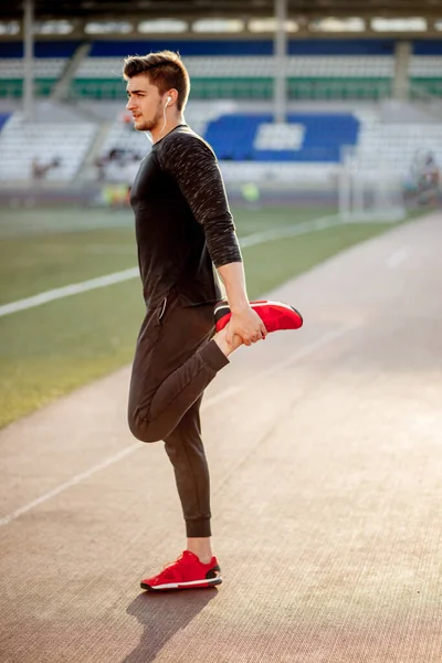 Man stretches the body before running on race track in stadium — Stock Photo, Image