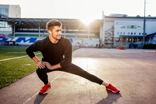 Man stretches the body before running on race track in stadium — Stock Photo, Image