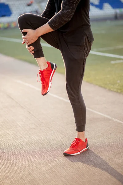 Man stretches the body before running on race track in stadium — Stock Photo, Image