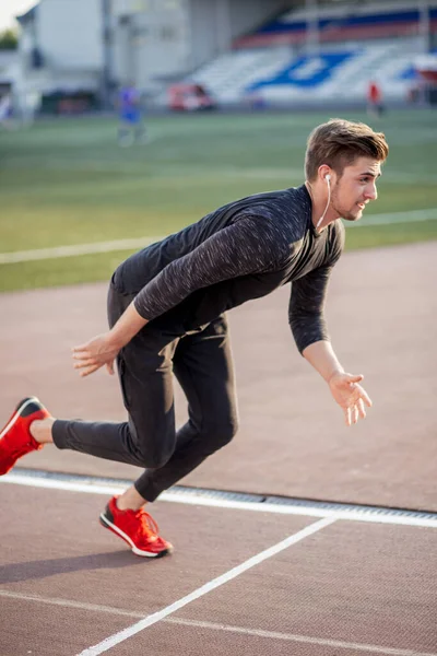 Atleta en ropa negra comenzando sprint en pista de running —  Fotos de Stock