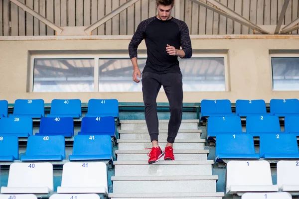 Hombre en forma vistiendo ropa negra corriendo arriba en el estadio deportivo —  Fotos de Stock