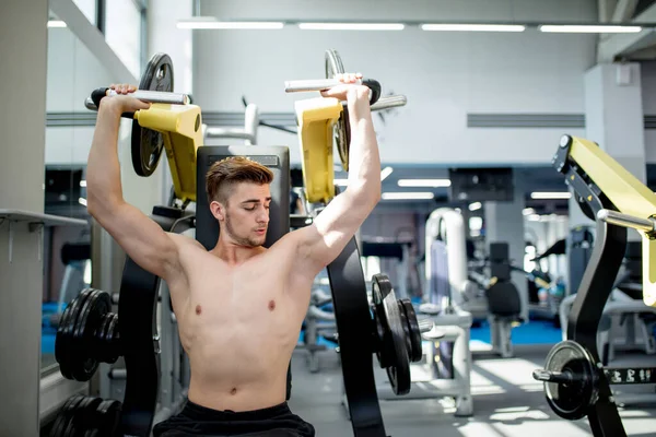 A young athlete trains in the gym. Bodybuilder pumping up upper body muscules. — Stock Photo, Image