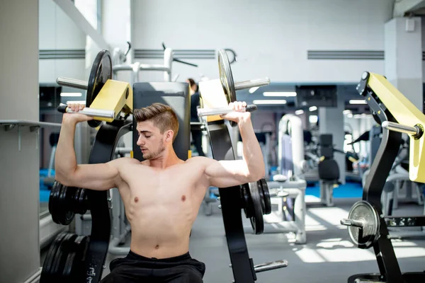 A young athlete trains in the gym. Bodybuilder pumping up upper body muscules. — Stock Photo, Image