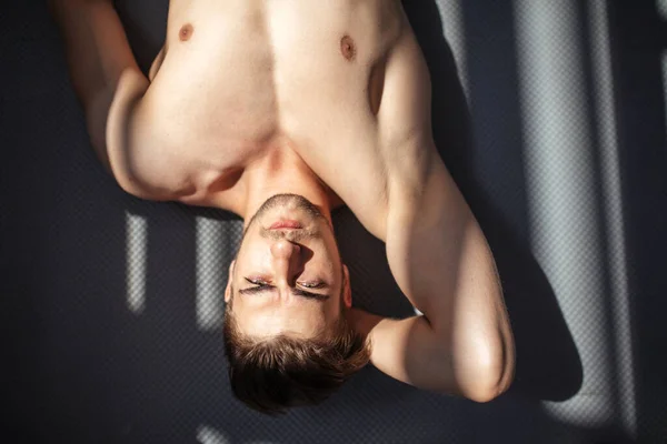 Kulturista ležící na podlaze v tmavé tělocvičně, se slunečními paprsky na těle . — Stock fotografie