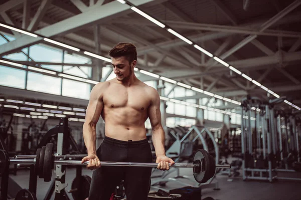 Jovem homem flexionando músculos com barbell no ginásio — Fotografia de Stock