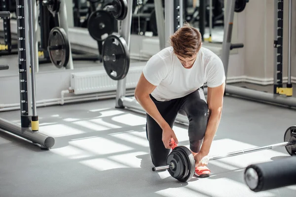 Muskularny mężczyzna nakładający ciężkie talerze na sztangę podczas treningu na siłowni — Zdjęcie stockowe