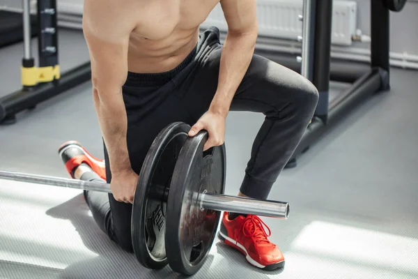 Homem muscular colocando pratos pesados na barra durante o treino no ginásio — Fotografia de Stock