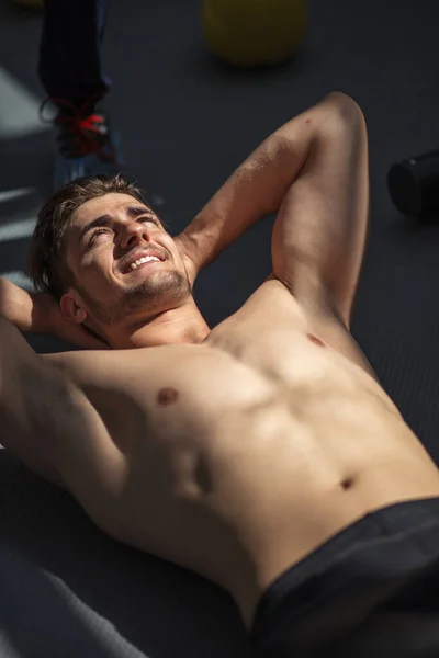 Atrakcyjny kulturysta bez koszulki odpoczywający w sali gimnastycznej, z umięśnionym tułowiem — Zdjęcie stockowe