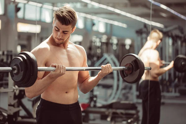 Young man flexing muscles with barbell in gym — Stock Photo, Image