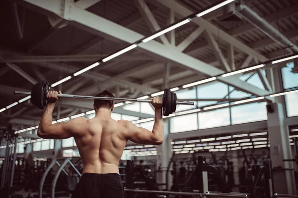 Rear view of young man with bar flexing muscles in gym — Stock Photo, Image