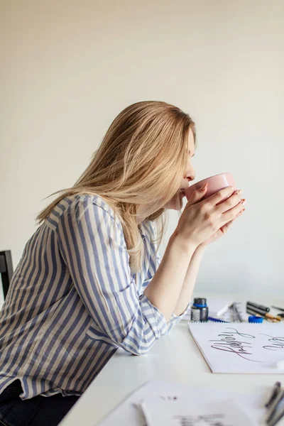 Zamknij się kobieta pisanie piękne notatki na papierze na białym biurku podczas picia kawy lub herbaty — Zdjęcie stockowe