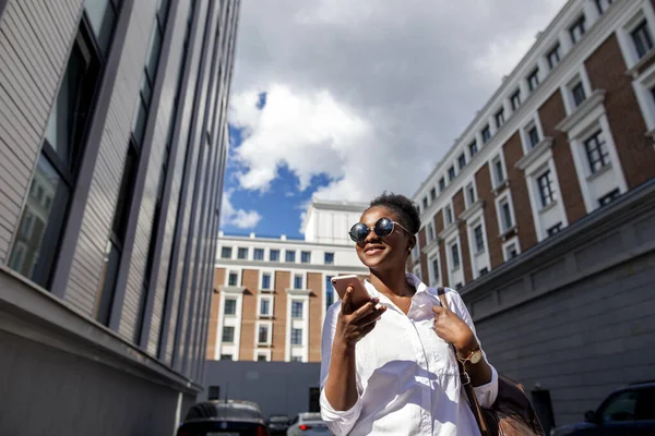 Africano mulher americana com mochila andando ao ar livre e falando no telefone móvel — Fotografia de Stock