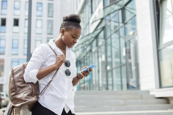 Afroamerikanerin mit Rucksack geht draußen spazieren und telefoniert — Stockfoto