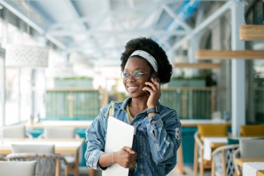 Afro saçlı, koyu tenli hippi kadın kafede akıllı telefondan konuşuyor..