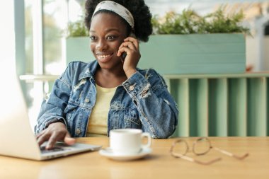 Kafede otururken, kıvırcık siyah saçlı genç Afrikalı kadın internetten alışveriş yapıyor..