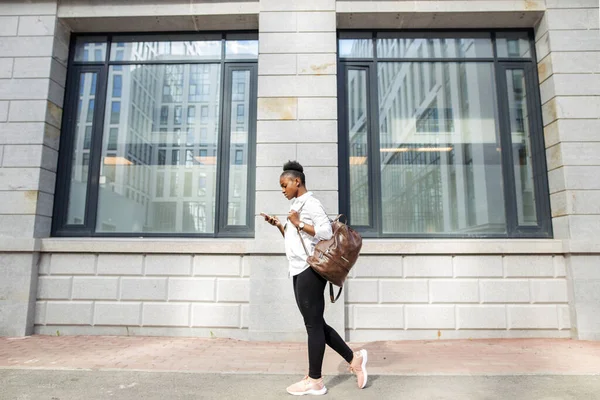 Sırt çantalı Afrikalı Amerikalı kadın dışarıda yürüyor ve cep telefonuyla konuşuyor. — Stok fotoğraf