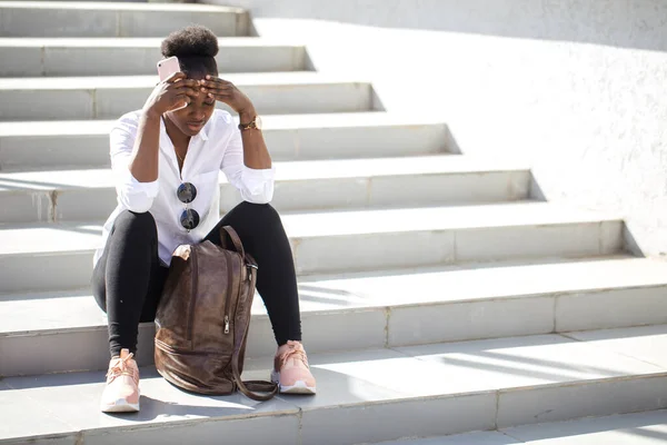 Afrikanerin benutzt Smartphone, während sie auf weißen Treppen im Freien sitzt. — Stockfoto