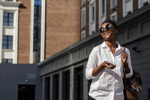 Afrikansk amerikansk kvinna med ryggsäck promenader utomhus och prata på mobiltelefon — Stockfoto