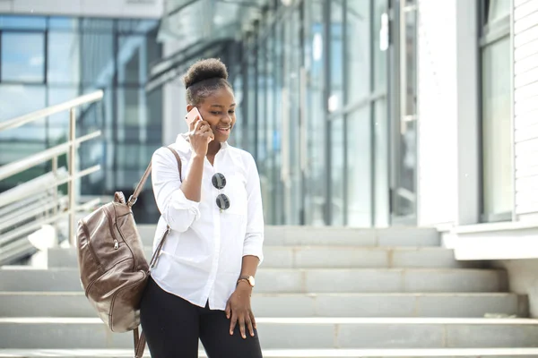 African american woman with backpack walking outdoor and talking on mobile phone — Stock Photo, Image