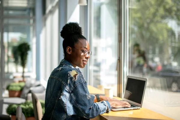 Donna afroamericana che utilizza il computer portatile mentre seduto al caffè, vista posteriore. — Foto Stock