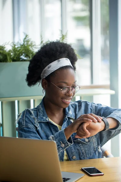 Mix-raced business woman looking at smart watch, working at office with tablet.