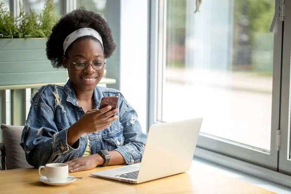 Mladá africká žena s kudrnaté tmavé vlasy nakupování on-line, zatímco sedí v kavárně. — Stock fotografie