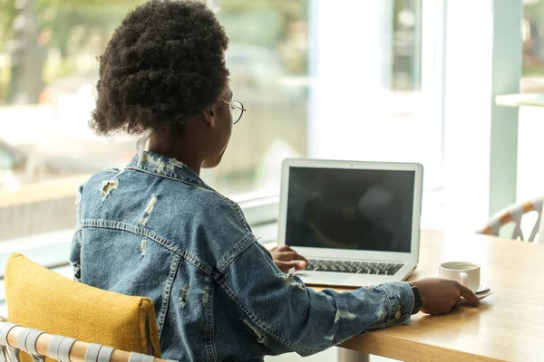 Mujer africana joven con pelo oscuro muy rizado de compras en línea mientras está sentado en la cafetería. — Foto de Stock