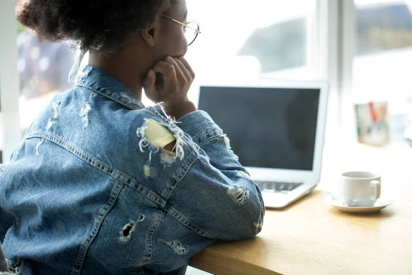 Afroamerikansk kvinna som använder laptop när hon sitter på caféet, bakifrån. — Stockfoto