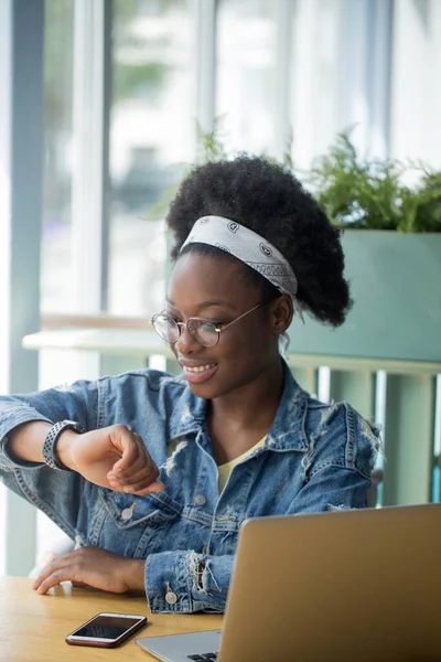 Mujer de negocios mixta mirando reloj inteligente, trabajando en la oficina con la tableta. — Foto de Stock