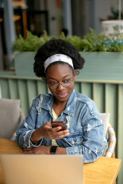 Mujer africana joven con pelo oscuro muy rizado de compras en línea mientras está sentado en la cafetería. —  Fotos de Stock