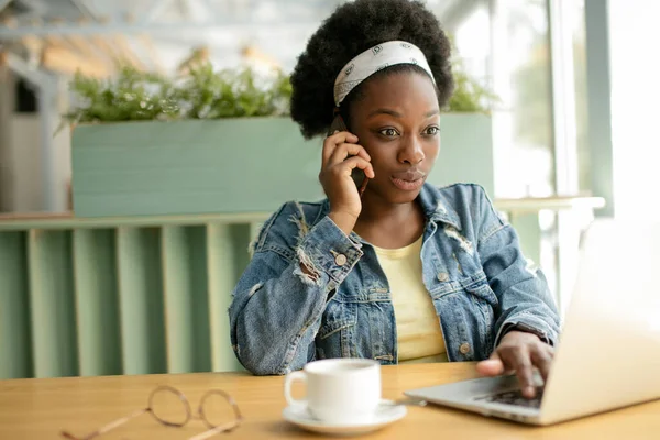 Mladá africká žena s kudrnaté tmavé vlasy nakupování on-line, zatímco sedí v kavárně. — Stock fotografie