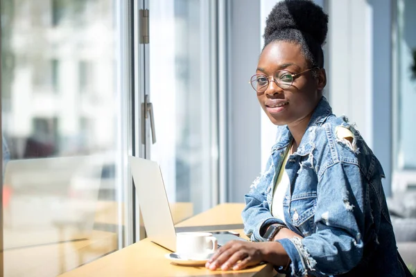 Ung afrikansk kvinna med burrigt mörkt hår shopping online medan du sitter på café. — Stockfoto