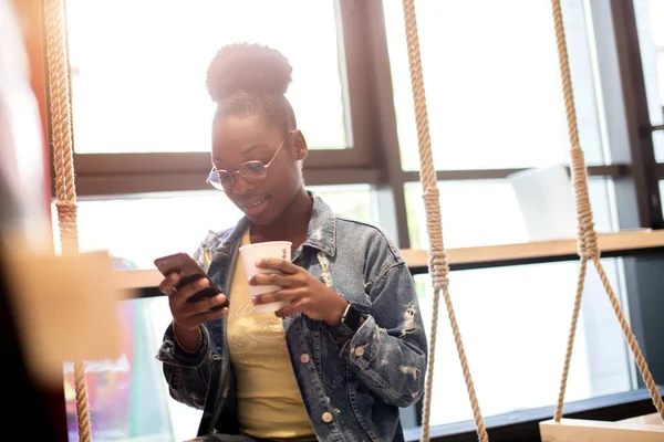 Hipster dunkelhäutige Frau mit Afro-Frisur unterhält sich mit Smartphone im Café. — Stockfoto