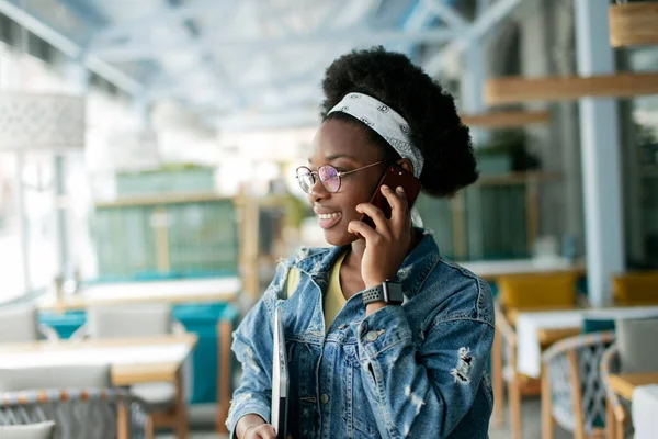 Hipster mulher de pele escura com penteado afro falando no telefone inteligente no café. — Fotografia de Stock