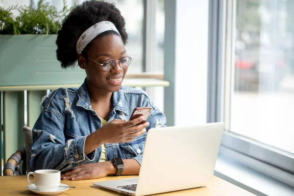 Mujer africana joven con pelo oscuro muy rizado de compras en línea mientras está sentado en la cafetería. — Foto de Stock