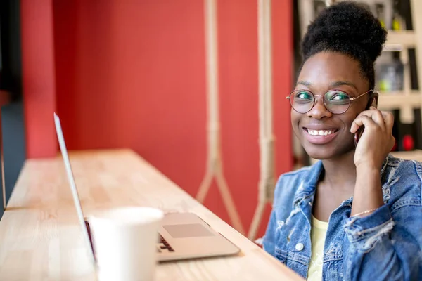 Kafede otururken, kıvırcık siyah saçlı genç Afrikalı kadın internetten alışveriş yapıyor.. — Stok fotoğraf