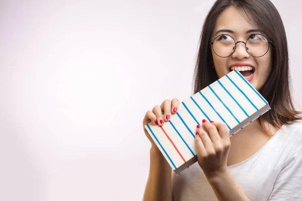 Perezosa asiática estudiante hembra mordiendo un libro, poco dispuesto a estudiar, aislado en estudio. —  Fotos de Stock